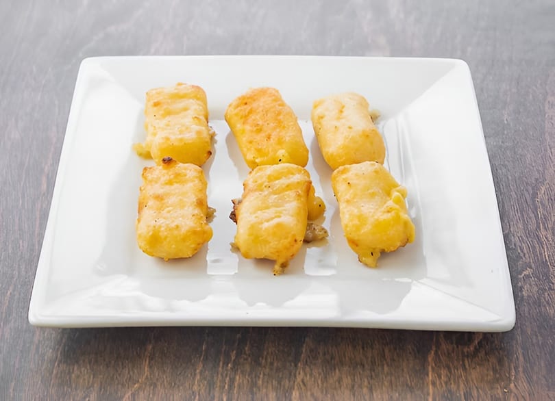 Six golden-brown fried cheese curds are arranged on a white rectangular plate.
