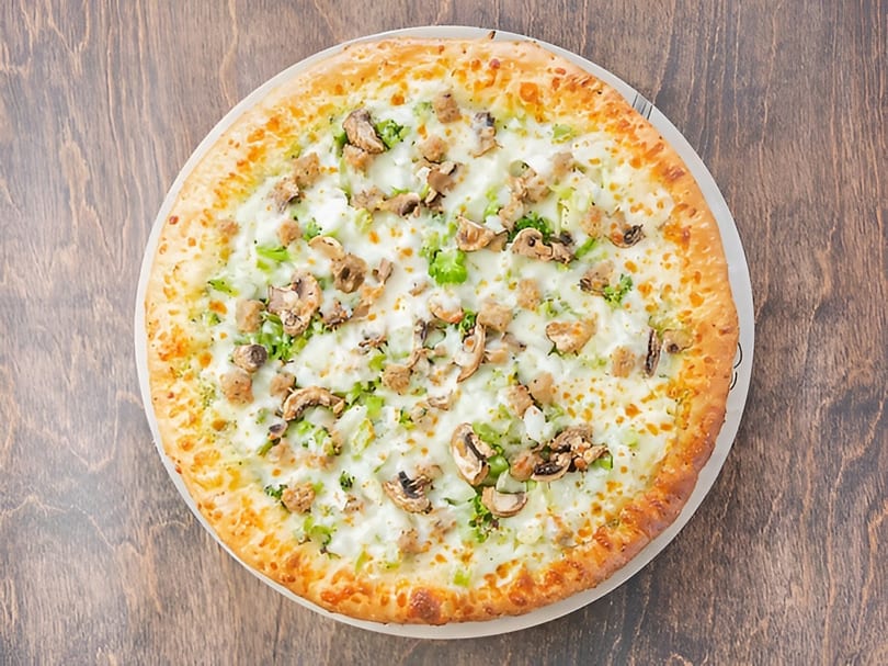 White pizza with broccoli, mushrooms, and sausage on a wooden table.